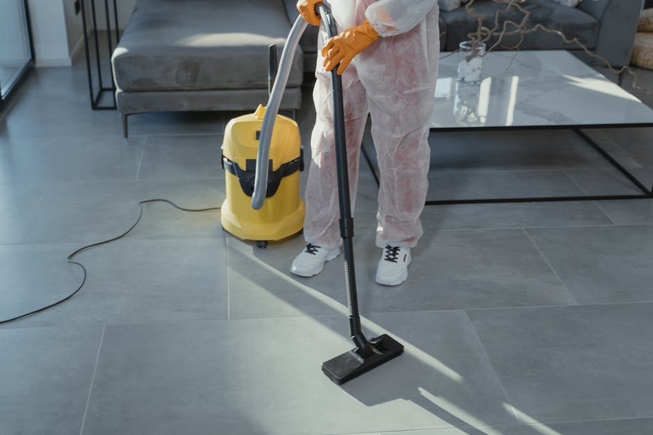A person wearing orange cleaning gloves is placing a lightbox sign with black letters spelling 'CLEANING HOME' on a table in a modern, well-lit room. The surface of the table appears smooth and clean, and the background shows a blurred interior with natural daylight coming in. This image visually represents domestic surface cleaning and deep cleaning activities performed by professionals like Hounslow Carpet Cleaners, highlighting the importance of proper hygiene and maintenance during end of tenancy cleaning processes in residential spaces.